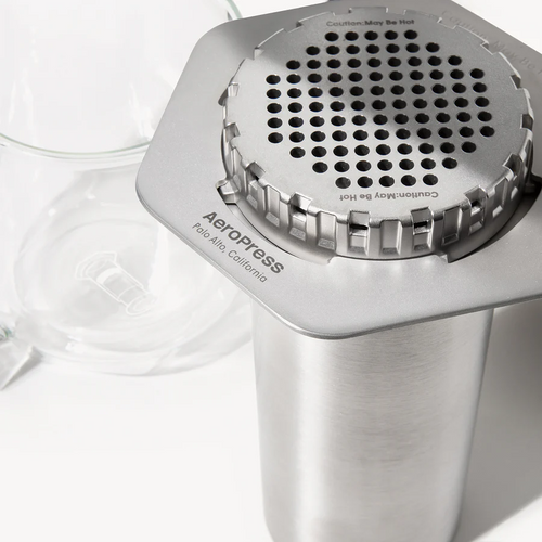 An AeroPress steel coffee maker with a stainless steel filter cap on a white background