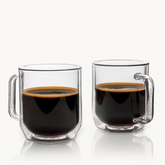 Two clear glass mugs filled with coffee on a white background