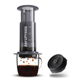 AeroPress original coffee maker brewing into a mug, next to a flow control filter cap