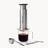AeroPress coffee maker with a glass of brewed coffee on a white background